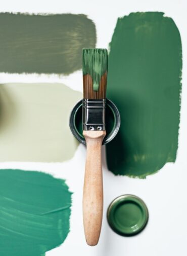 Una brocha de pintura sobre varios trazos de pintura verde en diferentes tonos de intensidad