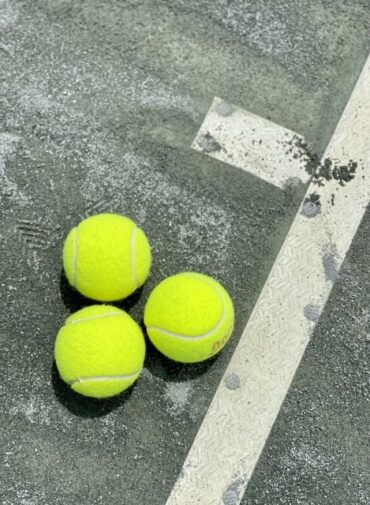 Tres pelotas de tenis sobre el suelo verde de una cancha de tenis desgastada por el uso